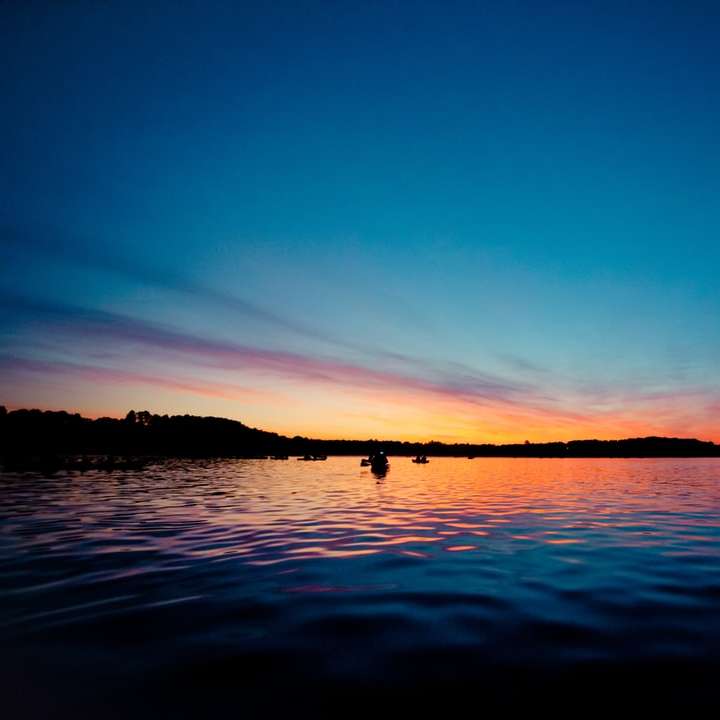 silhouette de personnes sur un plan d'eau au coucher du soleil puzzle en ligne