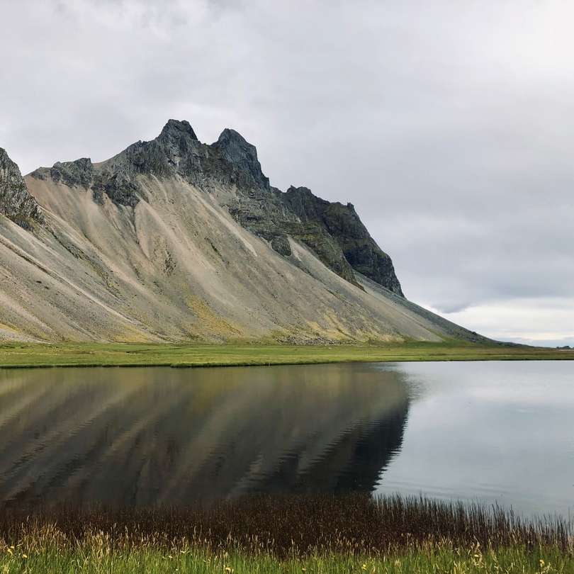 зелена тревна площ близо до езерото и планината под бели облаци плъзгащ се пъзел онлайн