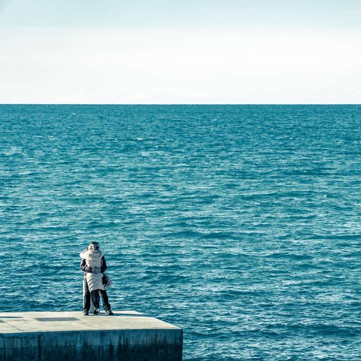 чоловік у чорній куртці, сидячи на бетонній лавці біля моря розсувний пазл онлайн