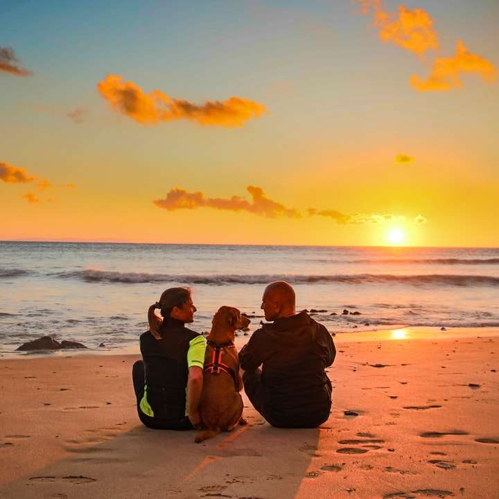 man and woman sitting on beach during sunset sliding puzzle online