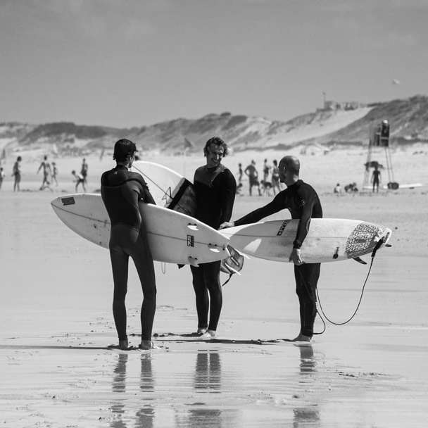 zdjęcie w skali szarości przedstawiające 2 mężczyzn i kobietę trzymających deskę surfingową puzzle online