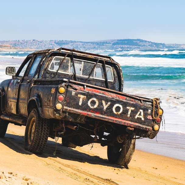 SUV preto na areia marrom perto do corpo d'água durante o dia puzzle deslizante online