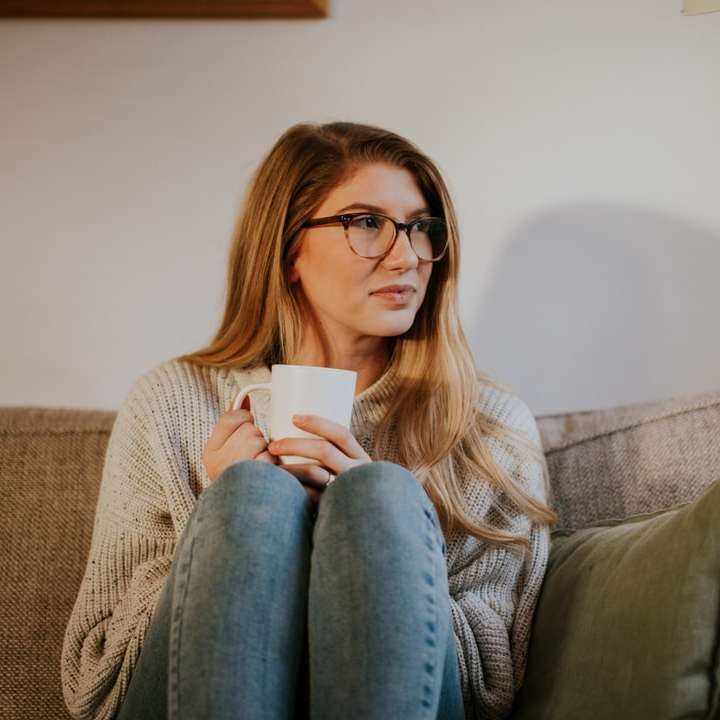 Frau in blauen Jeans, die auf grauem Sofa sitzt Schiebepuzzle online