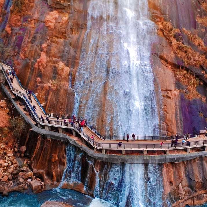 люди ходят по коричневому деревянному мосту над водопадами онлайн-пазл