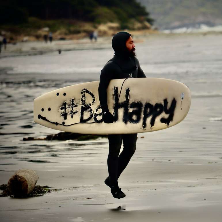 mężczyzna w czarnej bluzie z kapturem niosący białą deskę surfingową puzzle przesuwne online