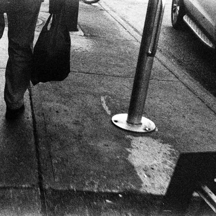 person i svarta byxor och svarta stövlar som står på trottoaren Pussel online