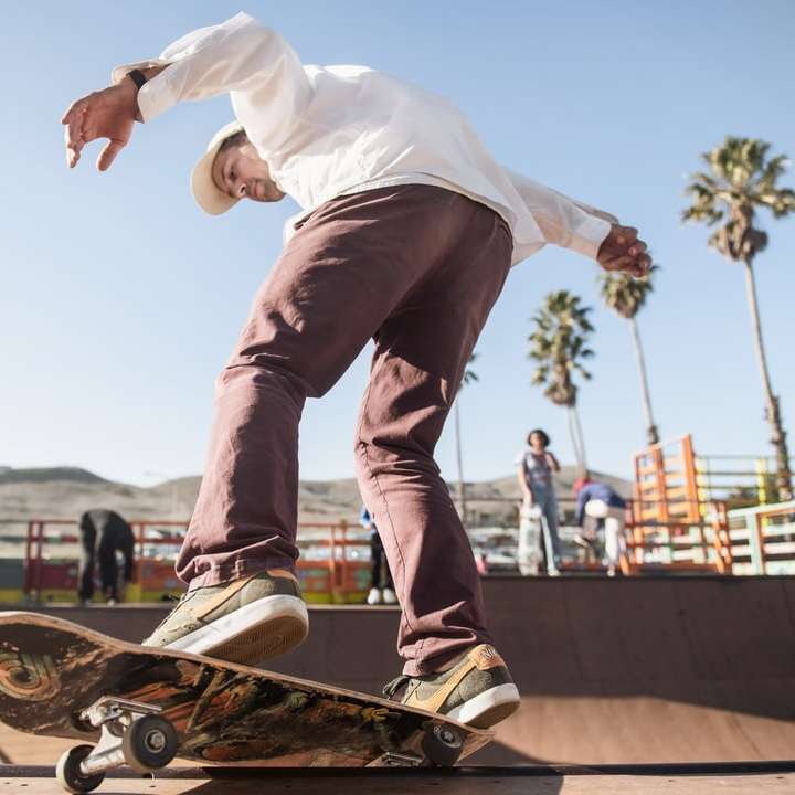 Мужчина в белой рубашке и коричневых штанах катается на скейтборде онлайн-пазл