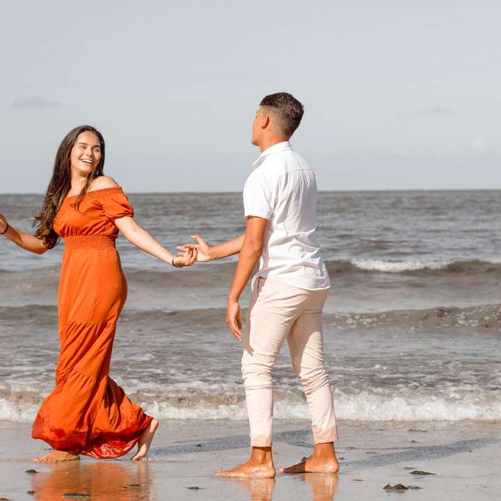 man and woman holding hands while walking on beach sliding puzzle online