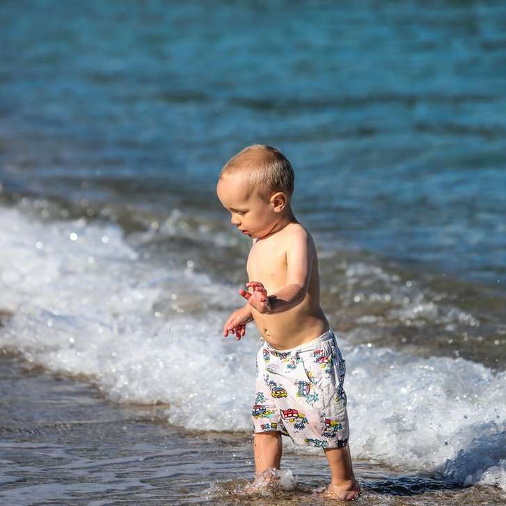 child in white and blue floral shorts standing on beach sliding puzzle online