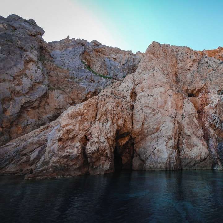 brązowa formacja skalna na błękitnym morzu pod błękitnym niebem puzzle przesuwne online