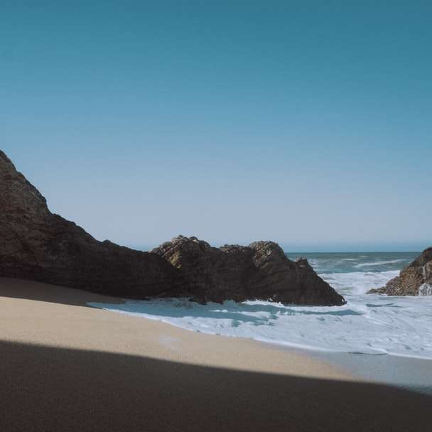 praia de areia marrom perto da montanha marrom sob céu azul puzzle online