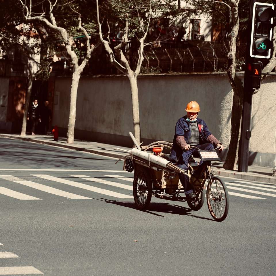 homem de jaqueta azul andando em um triciclo preto e vermelho na estrada puzzle deslizante online