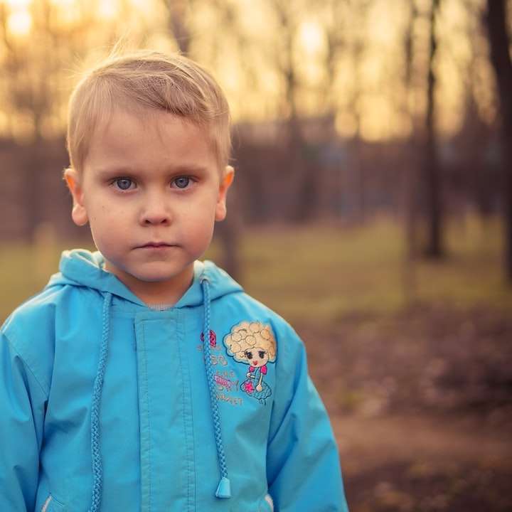 chłopiec w niebieskiej bluzie stojącej na brązowym polu w ciągu dnia puzzle online