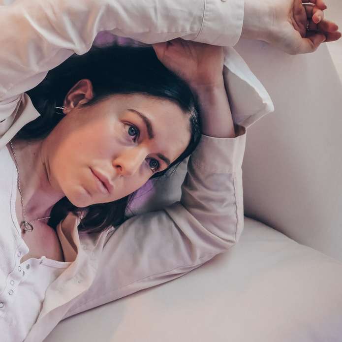 woman in white long sleeve shirt lying on bed sliding puzzle online