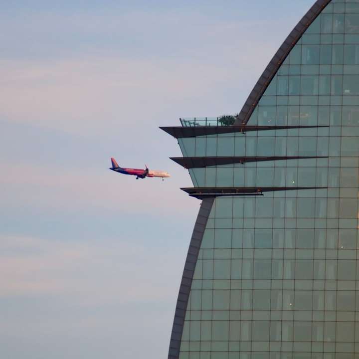 czerwony i biały samolot lecący nad szklanym budynkiem puzzle przesuwne online