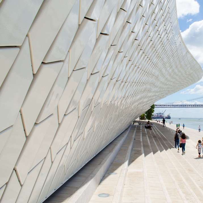 ludzie chodzą na biały betonowy most pod błękitnym niebem puzzle online