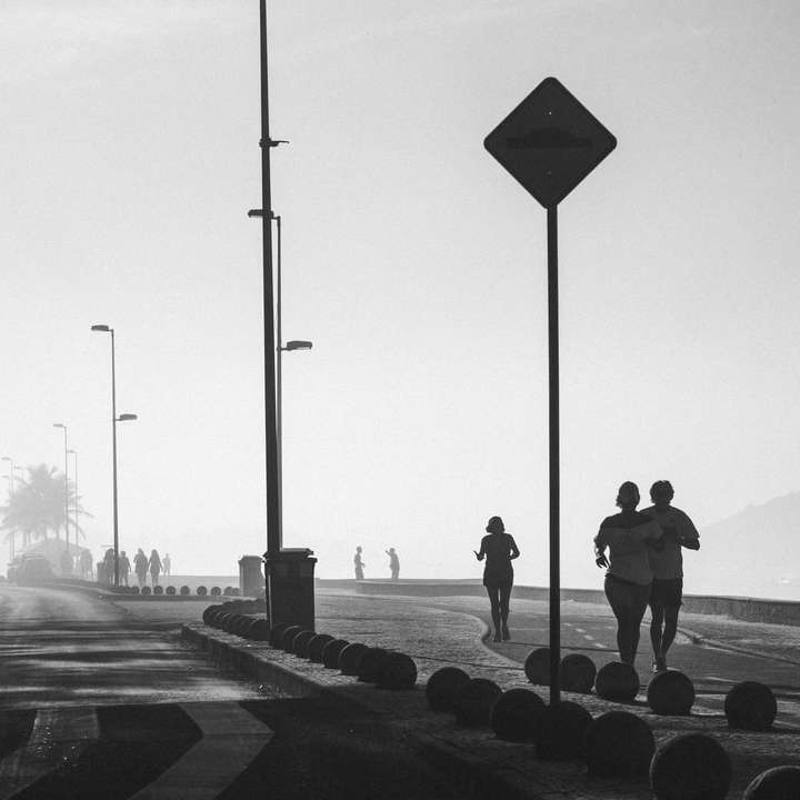 Foto en escala de grises de personas caminando en la acera cerca del cuerpo rompecabezas en línea
