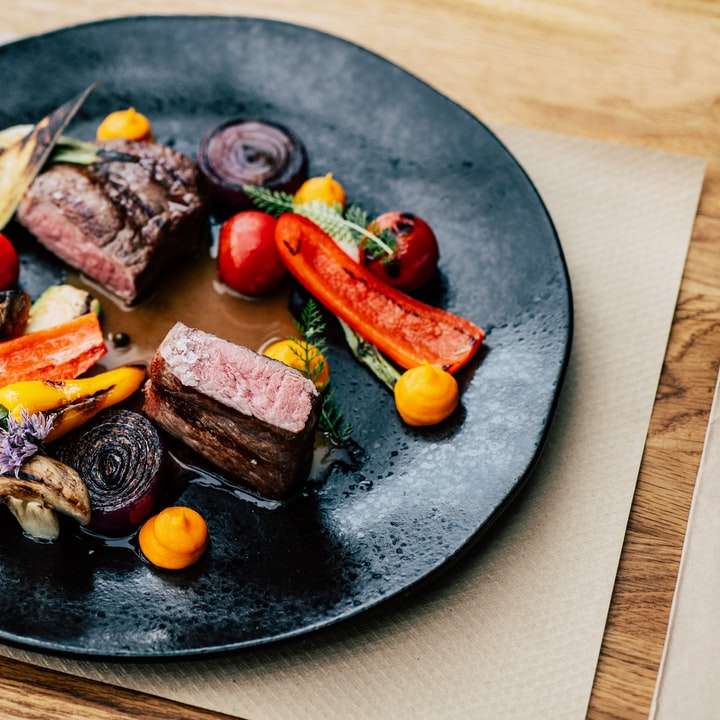 приготовленное мясо с овощами на черной круглой тарелке онлайн-пазл