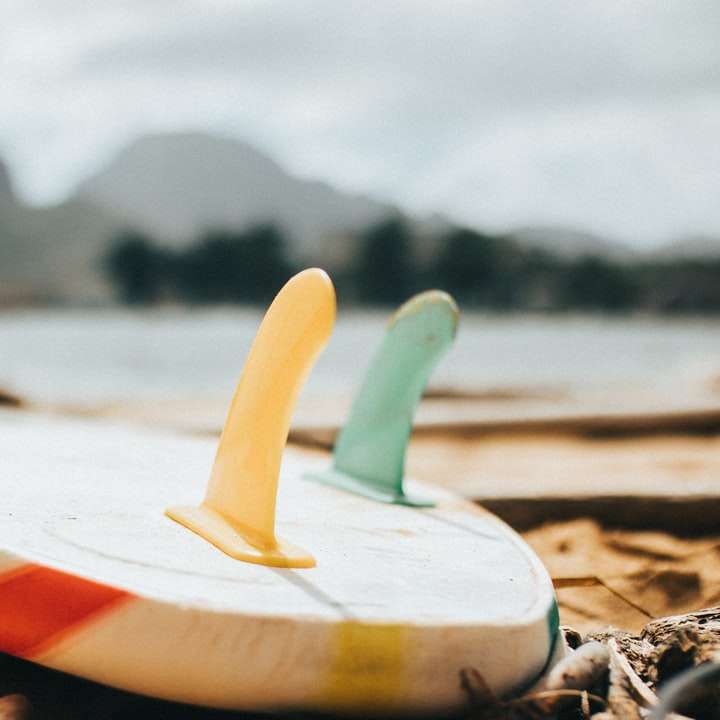 weißes und rotes Surfbrett am Strandufer während des Tages Schiebepuzzle online