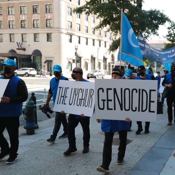 människor som står på trottoaren håller blå och vit banner Pussel online