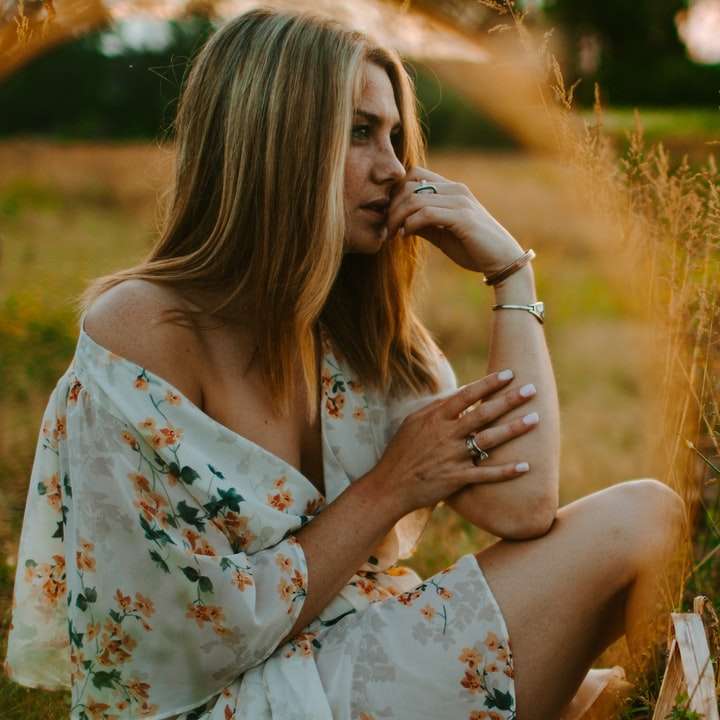 茶色の芝生のフィールドに座っている白い花柄のドレスの女性 オンラインパズル