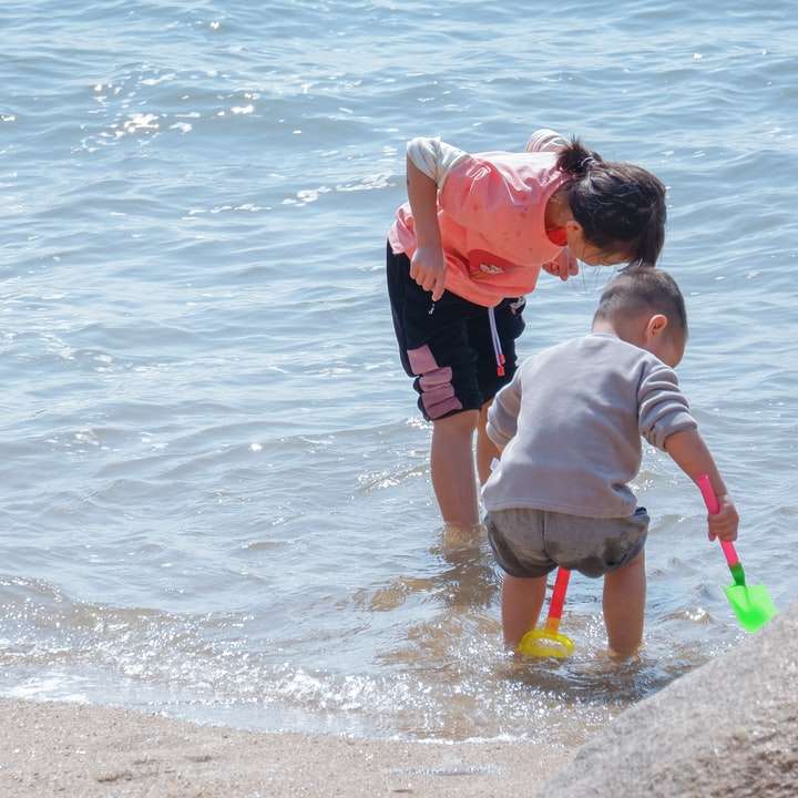 man in red shirt carrying child in white shirt on beach sliding puzzle online
