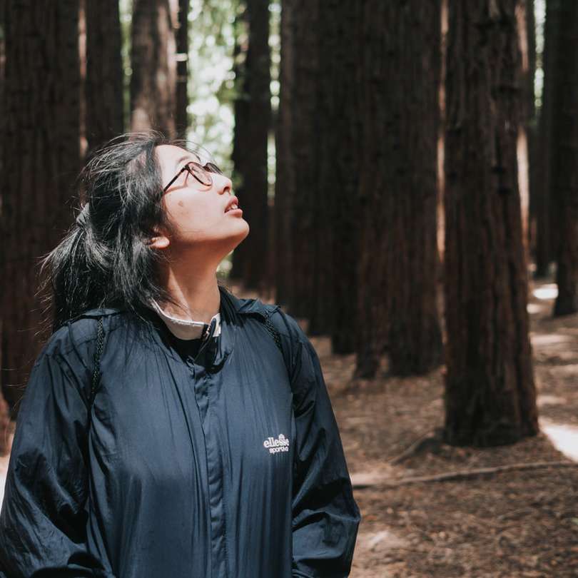 mulher de jaqueta preta em pé perto de árvores durante o dia puzzle online