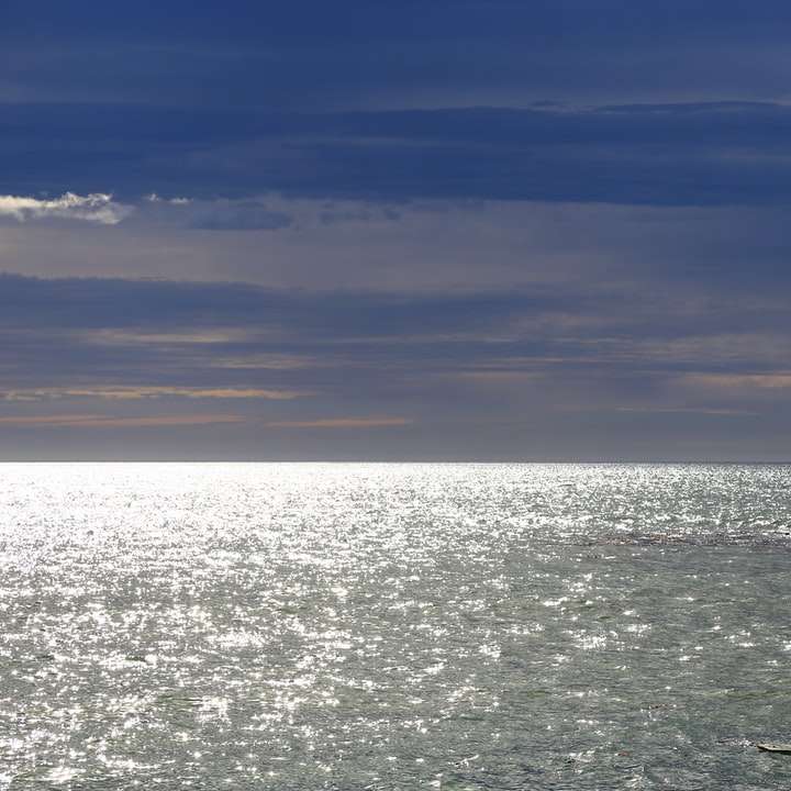 vagues de l'océan se brisant sur un rocher noir sous le ciel bleu puzzle en ligne
