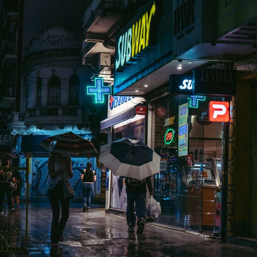 човек в черно палто, държащ чадър, ходещ по тротоара онлайн пъзел