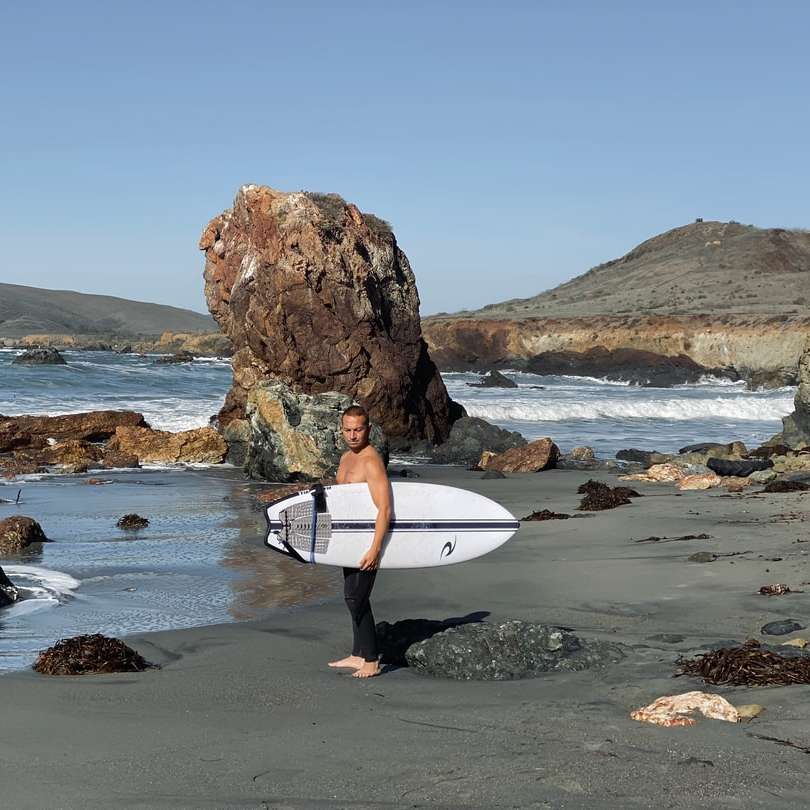 Mann im schwarzen Neoprenanzug, der weißes Surfbrett hält Online-Puzzle