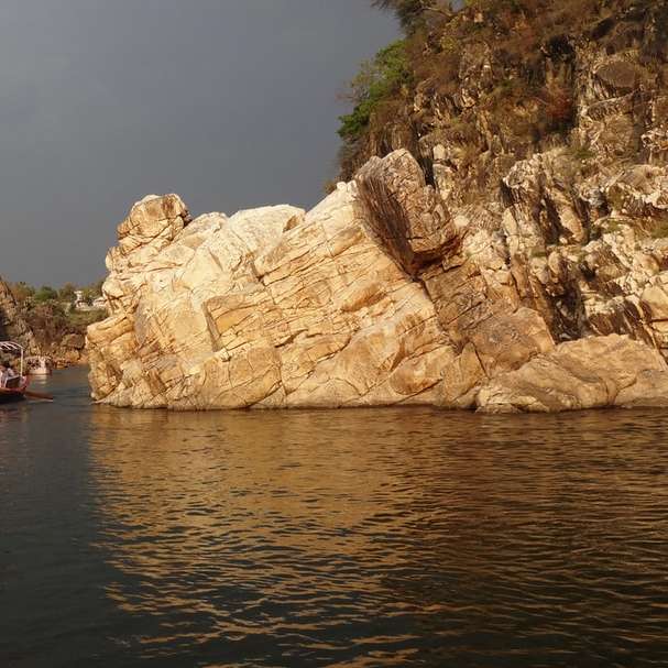 czerwona łódź na zbiorniku wodnym w pobliżu brunatnej formacji skalnej puzzle przesuwne online