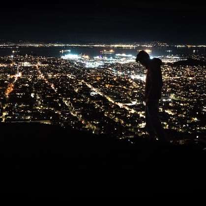 άντρας στέκεται στο έδαφος κοιτάζοντας τα φώτα της πόλης online παζλ