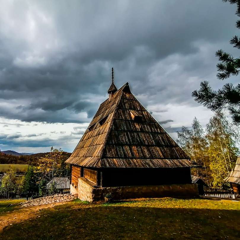 brązowy drewniany dom na zielonym polu trawy pod szarymi chmurami puzzle przesuwne online