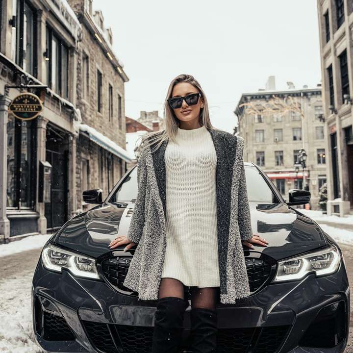 жінка в білому трикотажному шарфі стоїть біля чорного автомобіля онлайн пазл