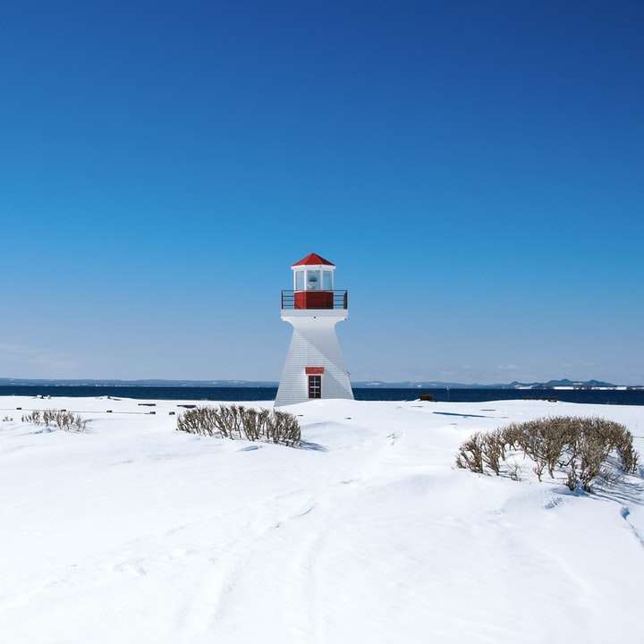 biała i czerwona latarnia morska na ziemi pokrytej śniegiem puzzle przesuwne online