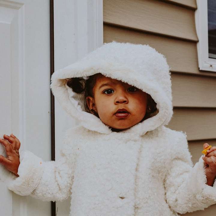 copil în haina albă de iarnă stând lângă ușa albă din lemn alunecare puzzle online