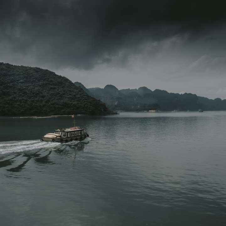 καφέ βάρκα στο σώμα του νερού κοντά στο βουνό κατά τη διάρκεια της ημέρας συρόμενο παζλ online