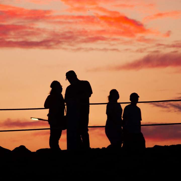 silueta de personas de pie sobre una roca durante la puesta de sol rompecabezas en línea