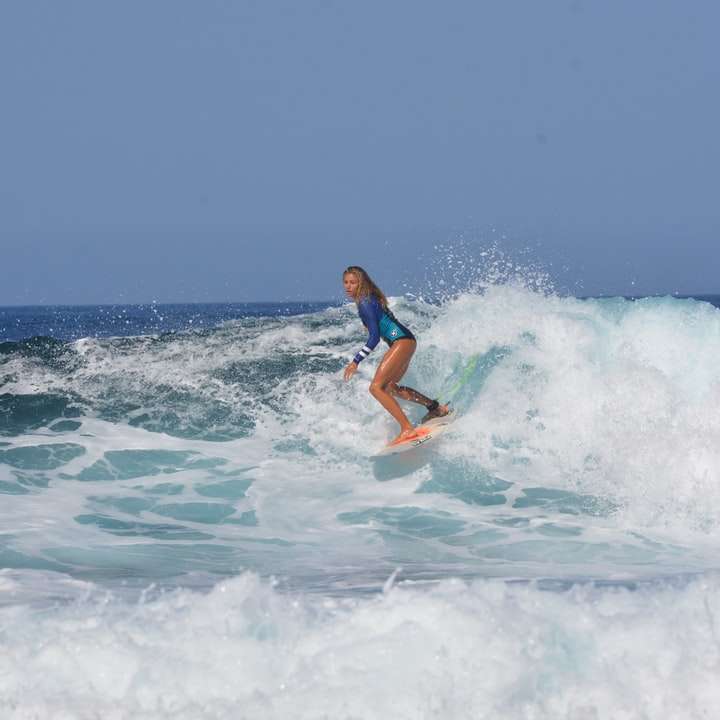 mulher de biquíni azul e branco surfando nas ondas do mar puzzle deslizante online