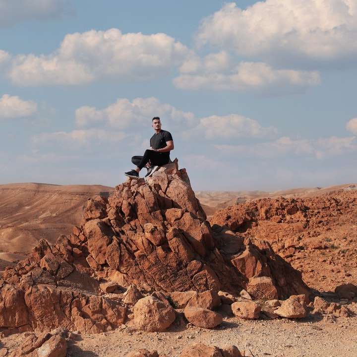 man in zwarte jas zittend op rotsformatie overdag schuifpuzzel online