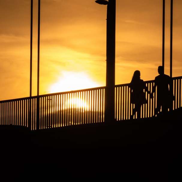 silueta de personas de pie en el puente durante la puesta de sol puzzle deslizante online