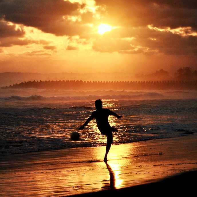 mężczyzna w czarnej koszuli i spodenkach na plaży podczas zachodu słońca puzzle przesuwne online