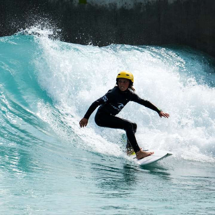 Mann im schwarzen Neoprenanzug, der gelbes Surfbrett auf Wasser reitet Schiebepuzzle online