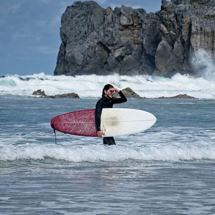 homem de terno preto segurando uma prancha de surf vermelha nas ondas do mar puzzle deslizante online