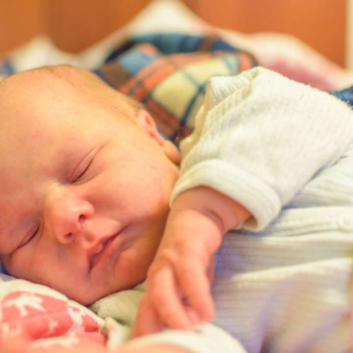 bebé en onesie blanco y azul acostado en la cama rompecabezas en línea