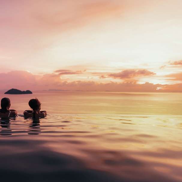 Silhueta de 2 pessoa no corpo da água durante o pôr do sol puzzle deslizante online