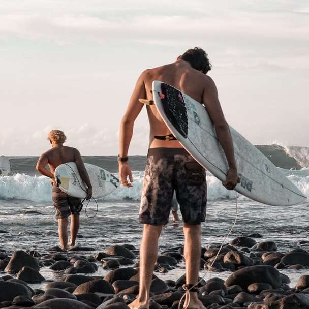 2 donne che tengono il surf in piedi sulla riva rocciosa puzzle online