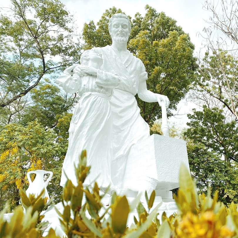 vit ängel staty nära gröna träd under dagtid Pussel online