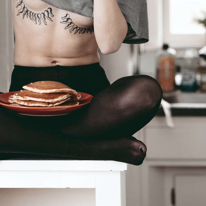 Kvinna i svart panty och brassiere knäböjer på svart säng glidande pussel online