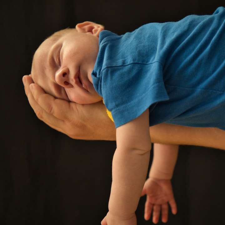 Baby i blå skjorta som ligger på brunt trägolv glidande pussel online